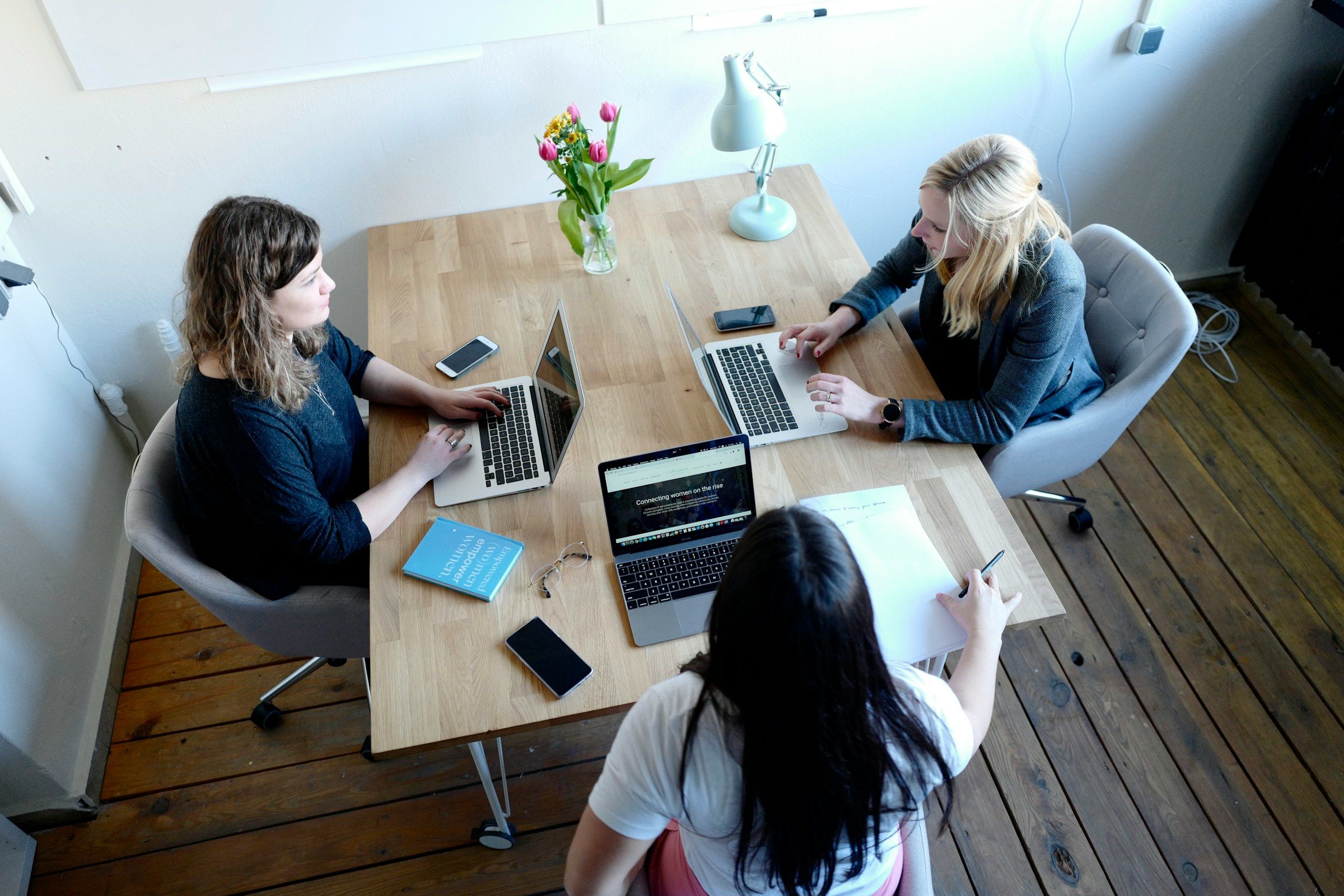 Vue du dessus : trois collègues travaillent ensemble autour d’une table, ordinateurs ouverts.